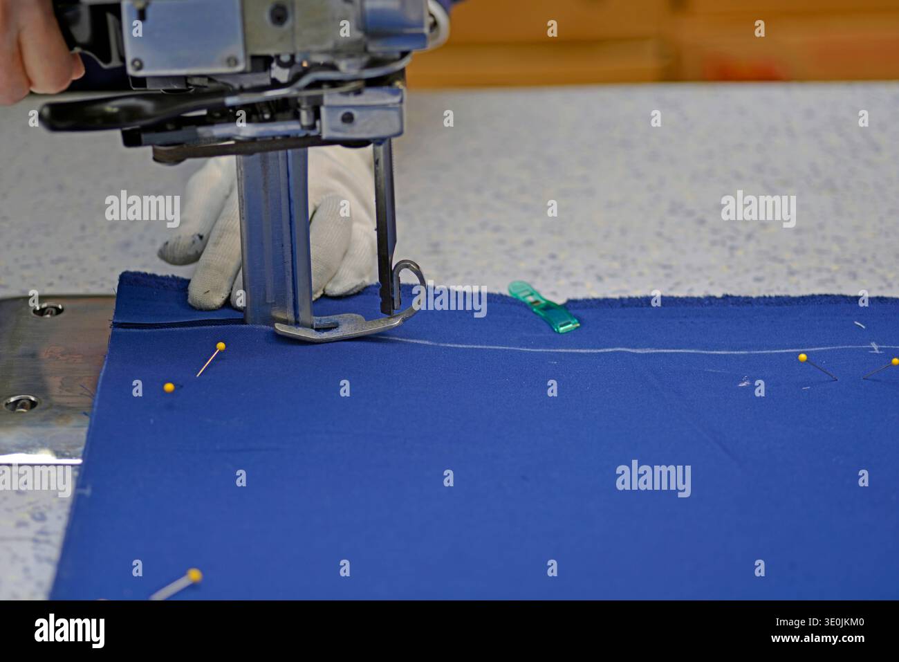 Una taglierina elettrica viene utilizzata per ritagliare i motivi su più strati di tessuto trapano in poliestere di cotone per pantaloni Foto Stock