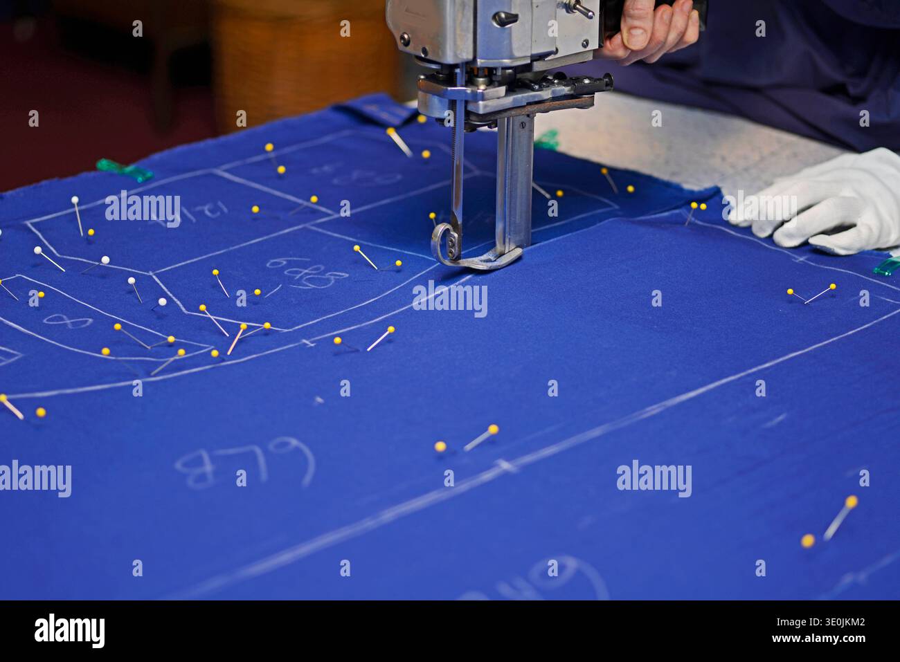 Una taglierina elettrica viene utilizzata per ritagliare i motivi su più strati di tessuto trapano in poliestere di cotone per pantaloni Foto Stock