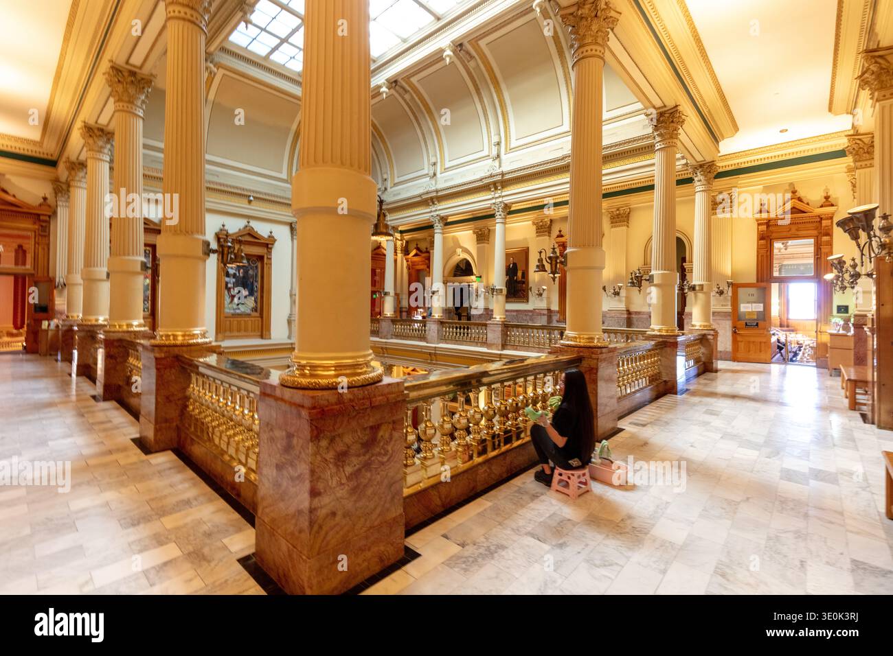 Denver, Colorado, USA - 3 marzo 2026: Una donna pulisce le ringhiere di ottone lungo una scala all'interno dello storico edificio del Campidoglio dello stato del Colorado a Denv Foto Stock