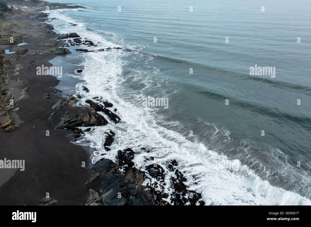 Vista aerea panoramica delle onde che si infrangono sulla costa rocciosa lungo l'oceano durante una giornata nuvolosa Foto Stock