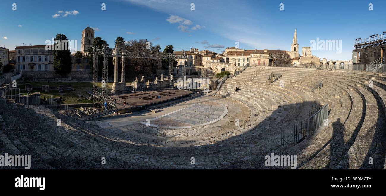 Vista panoramica del Teatro Romano di Arles con posti a sedere in pietra, rovine del palcoscenico e paesaggio urbano circostante sotto un cielo limpido ad Arles, Provenza, Francia. Foto Stock