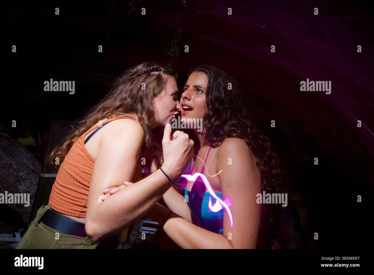 Ragazza che sussurra qualcosa nell'orecchio della sua amica in un posto notturno Foto Stock