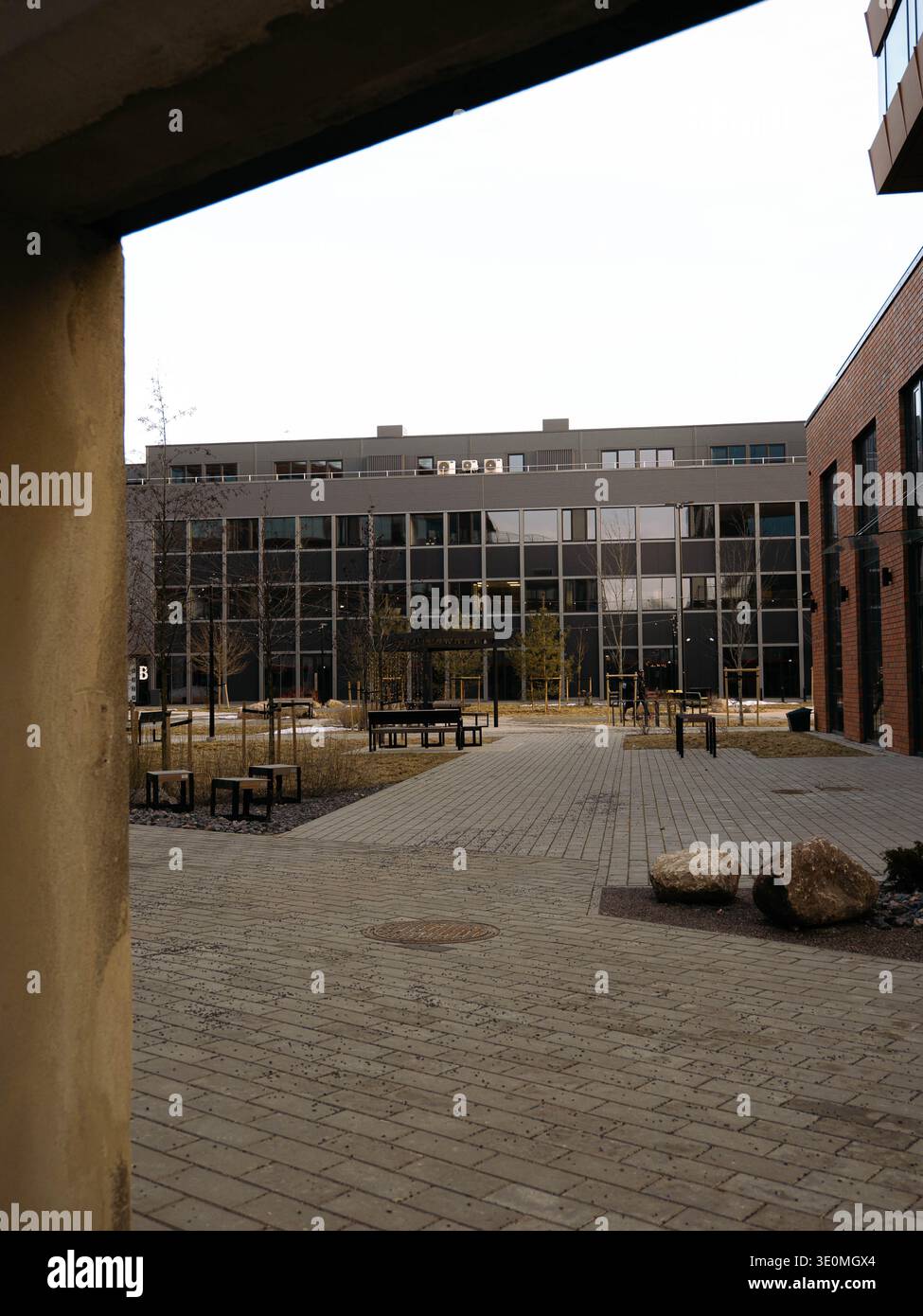 Moderno e vuoto cortile con edificio in vetro, facciata in mattoni rossi e massi di granito in inverno a Tallinn Foto Stock