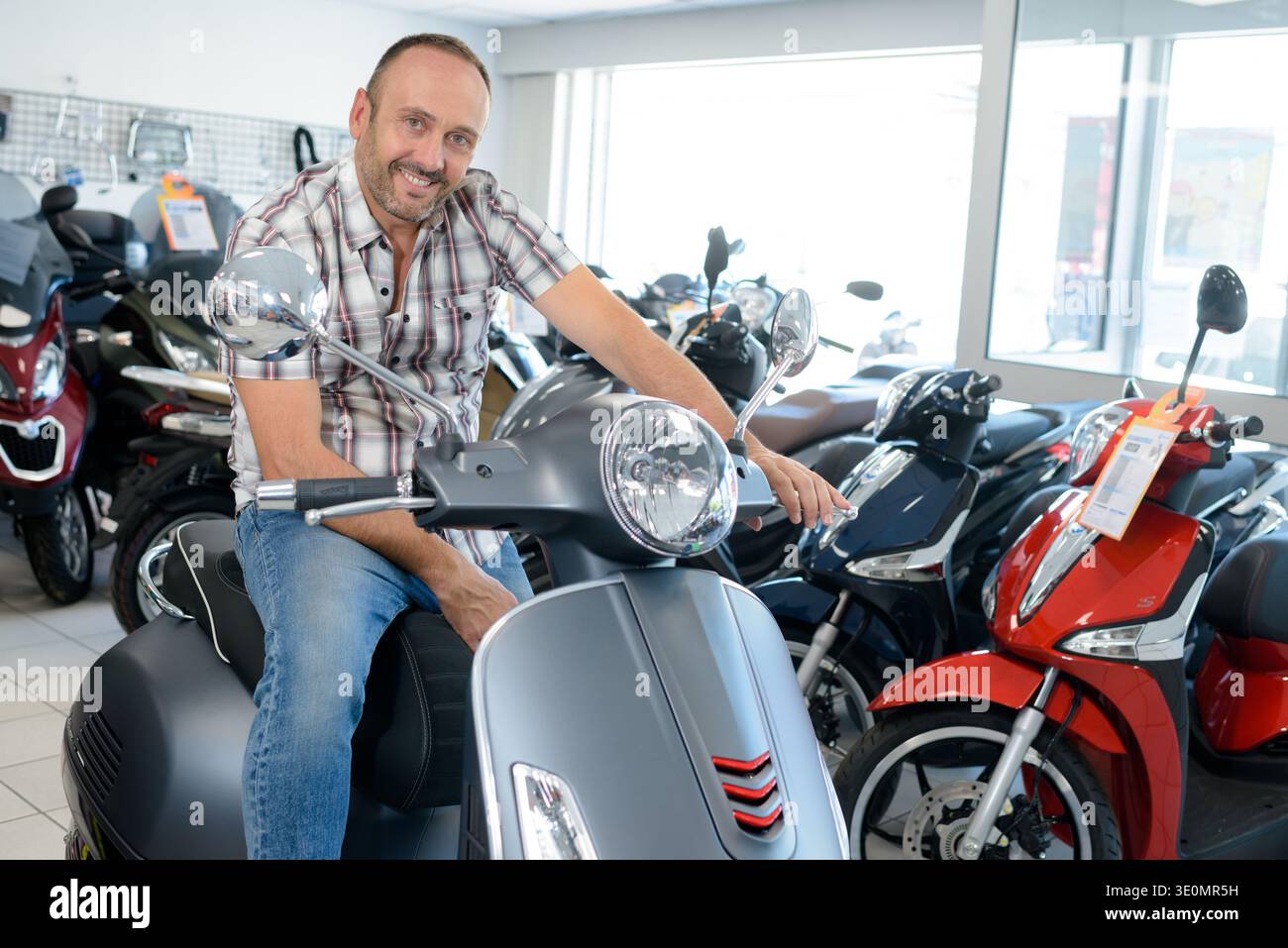 uomo seduto su uno scooter moderno in uno showroom di un concessionario Foto Stock