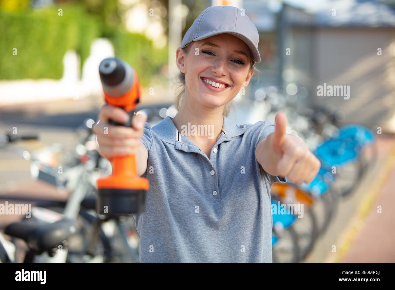 donna sorridente con la macchina da trapano che mostra il pollice in su Foto Stock