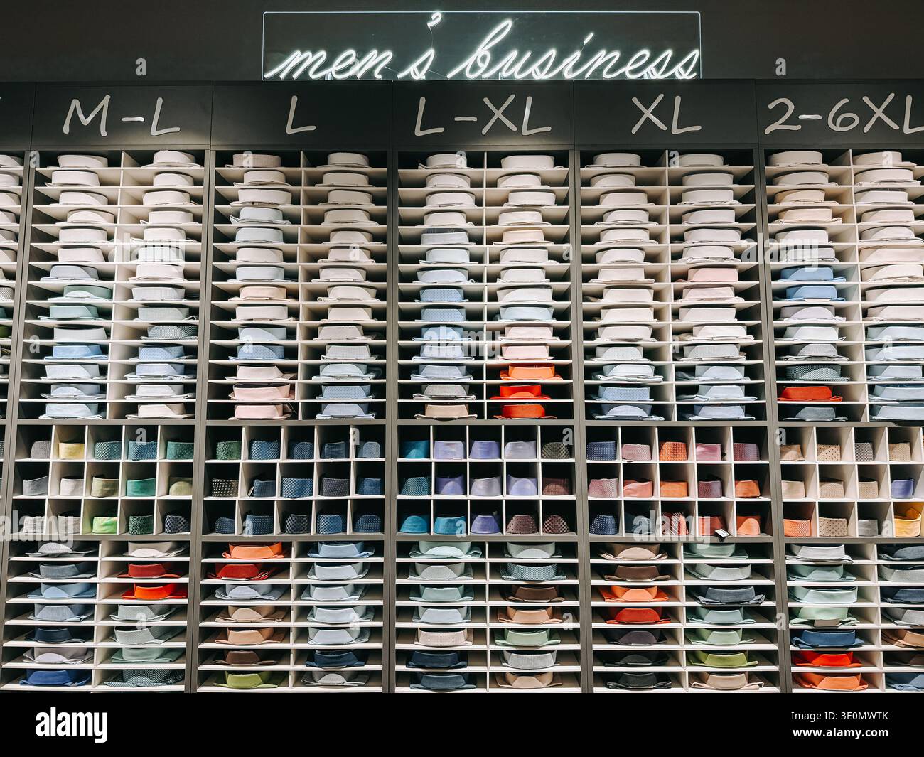 Riga, Lettonia - 12 marzo 2026: Camicie da uomo organizzate in base alle dimensioni in un moderno negozio di abbigliamento. Camicie piegate colorate in shel Foto Stock
