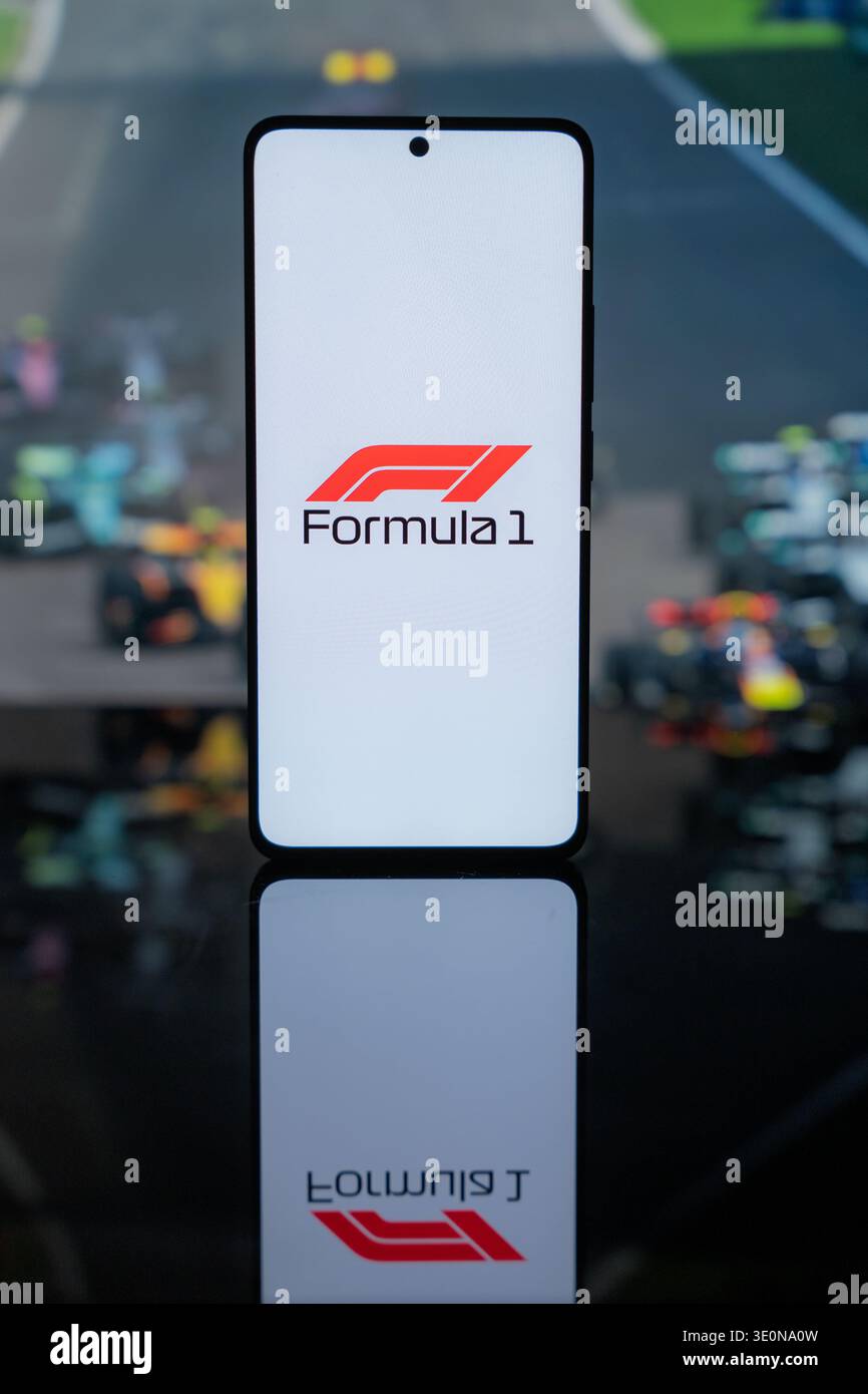 Il logo ufficiale di Formula 1 su uno schermo bianco, sullo sfondo sfocato delle auto da corsa di F1 su un tracciato, che rappresenta lo sport motoristico professionale Foto Stock
