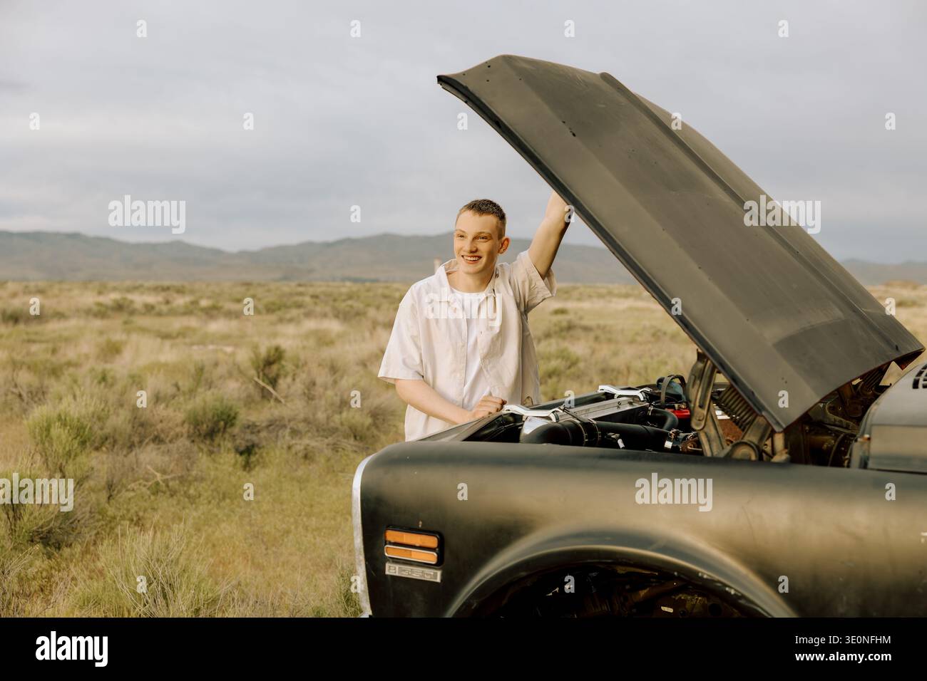 Un giovane sorridente che controlla il motore nel paesaggio rurale Foto Stock
