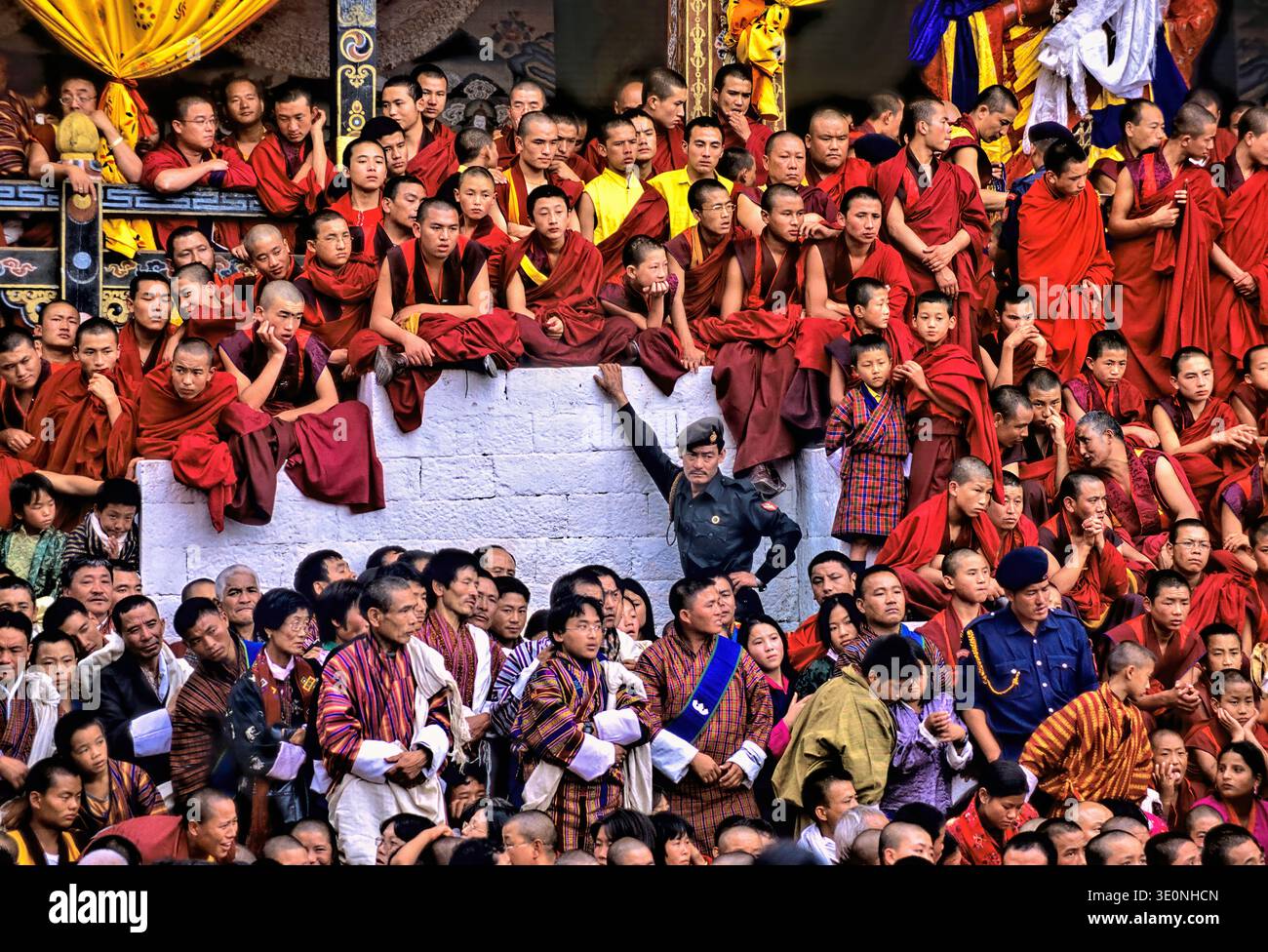 I monaci e le persone locali del Bhutan si riuniscono in abiti tradizionali per osservare una cerimonia religiosa. Si trovano a diversi livelli nella folla. Foto Stock