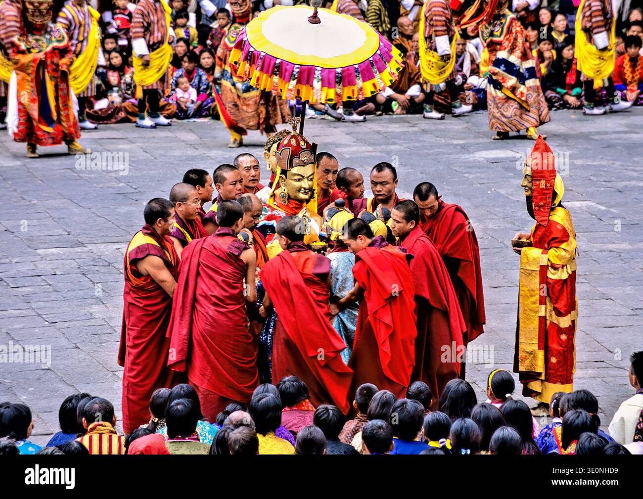 I monaci buddisti in abiti rossi eseguono una cerimonia intorno a una statua dorata durante un festival in Bhutan, mentre molti devoti guardano da vicino. Foto Stock