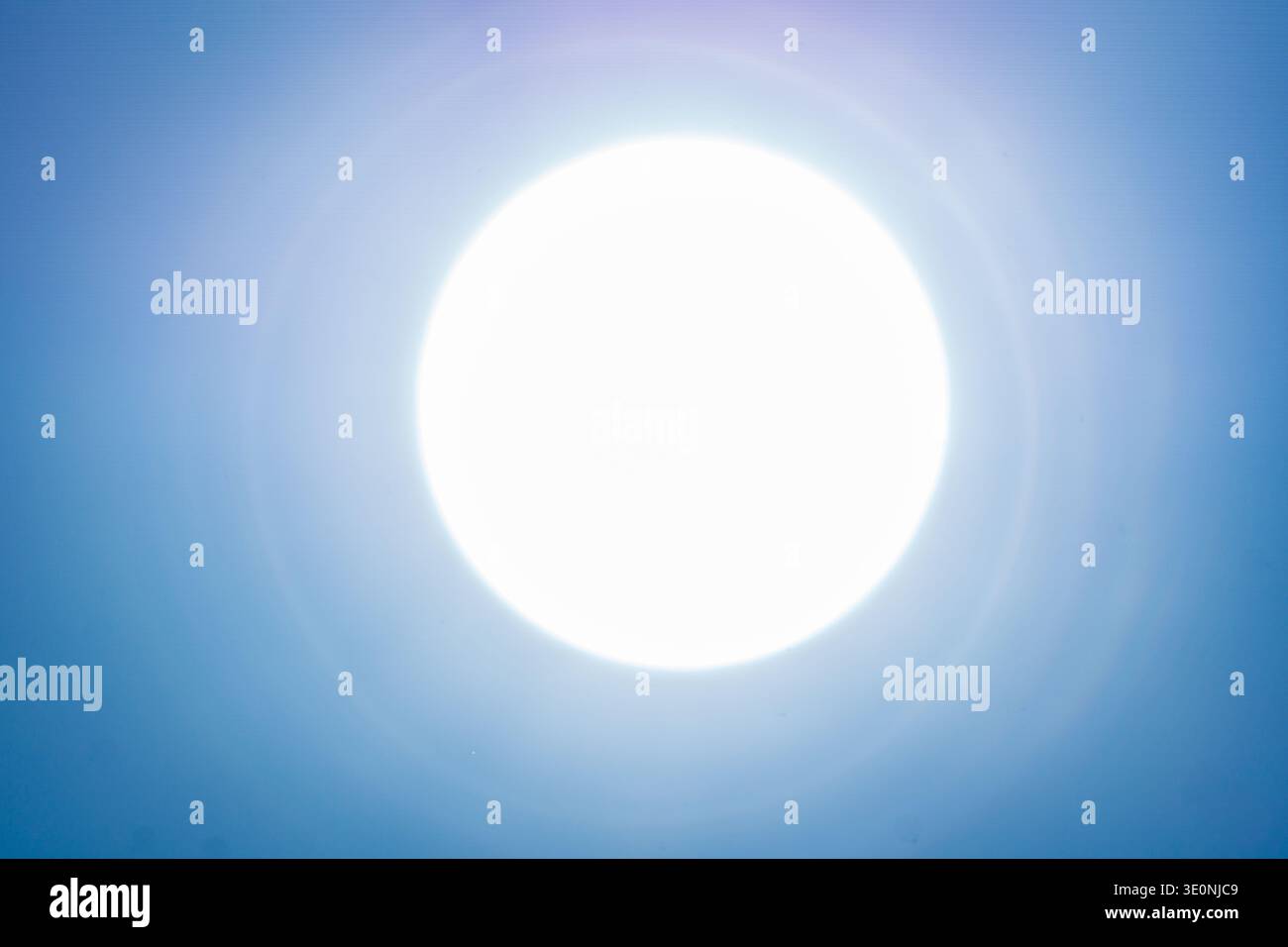 Vista minimalista del sole luminoso circondata da un soffice alone in un cielo azzurro. Foto Stock