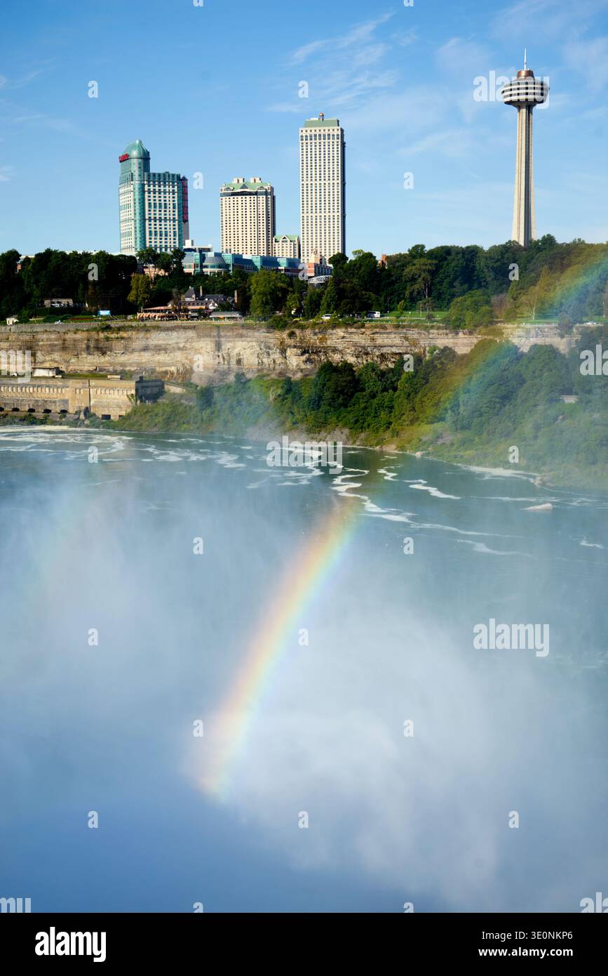 Un vivace arcobaleno attraversa la nebbia delle Cascate del Niagara, Ontario, Canada, con la Skylon Tower e lo skyline della città sullo sfondo. Foto Stock