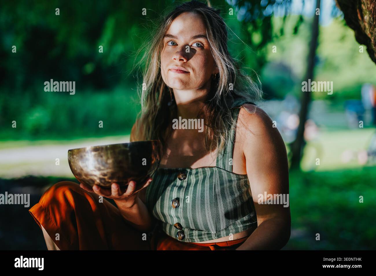 Giovane donna che tiene una ciotola per cantare gli ottoni all'aperto in un parco illuminato dal sole con gli amici dei Paesi Bassi Foto Stock