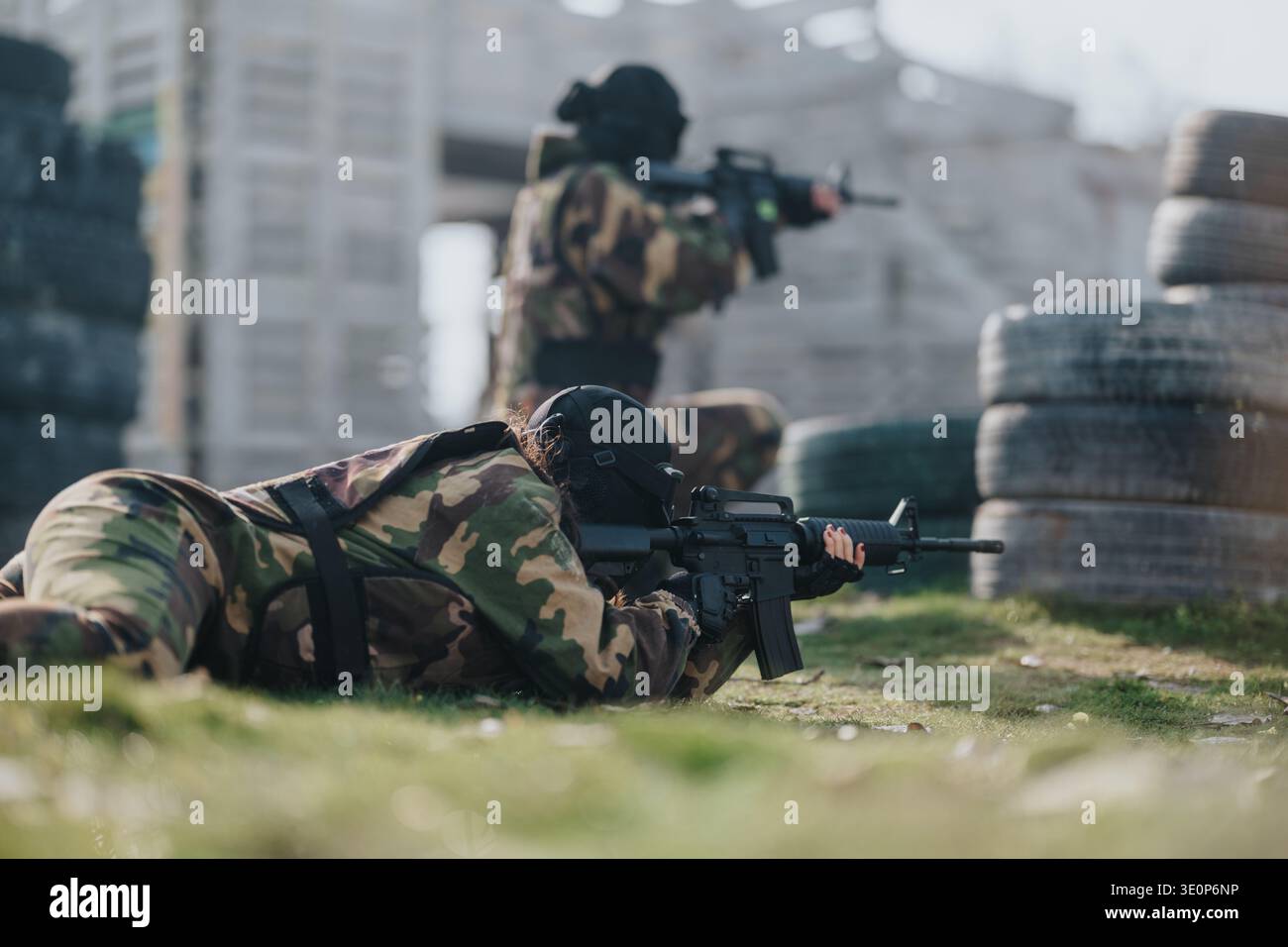 Soldati in camuffamento che giacciono inclini con fucili durante la battaglia Paintball dietro barriere e pneumatici Foto Stock