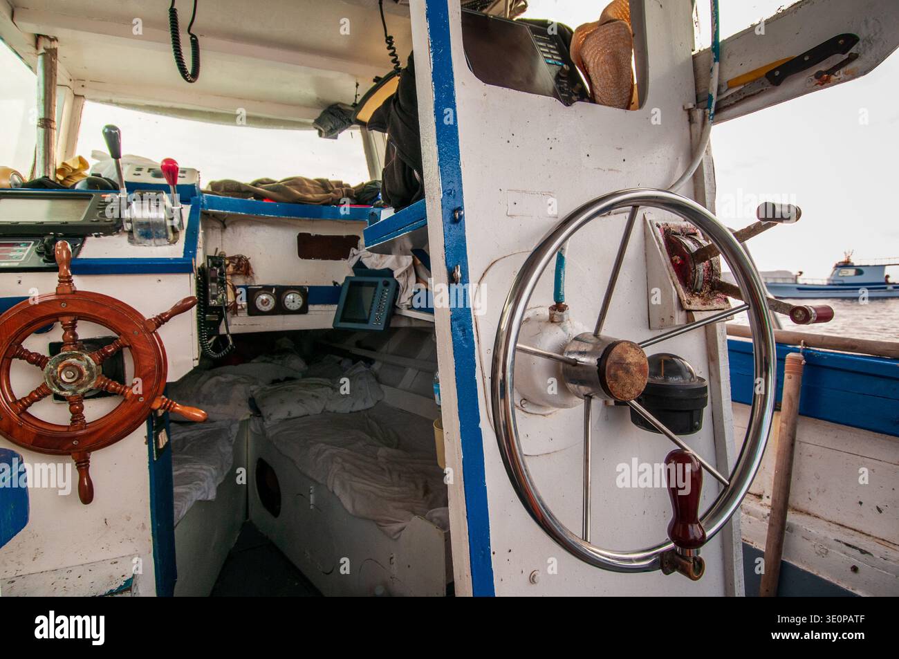 Vista del ponte di una barca da pesca con un volante in legno e uno moderno in acciaio inossidabile. L'interno include i monitor GPS, il comando dell'acceleratore Foto Stock