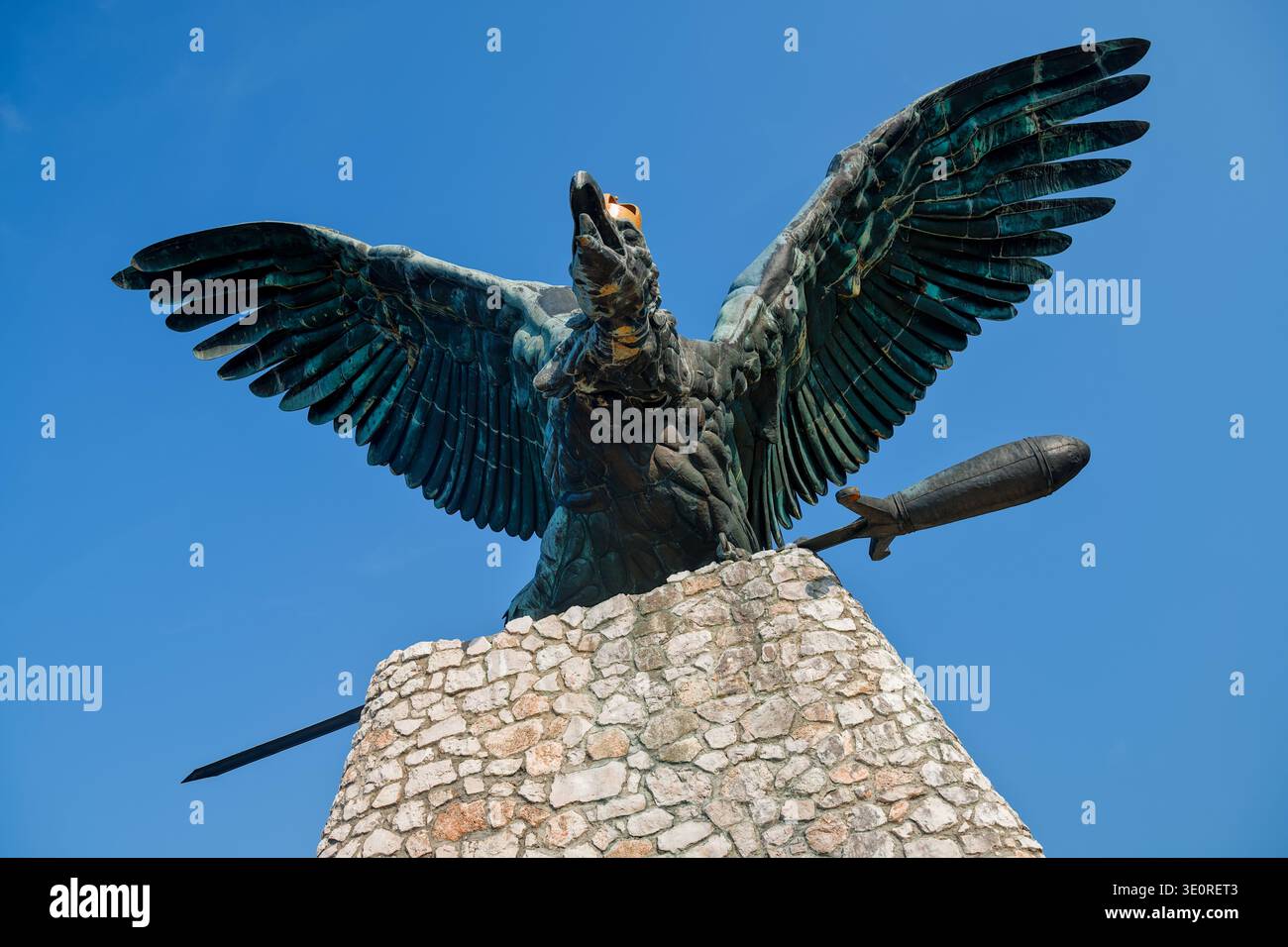 Vista simmetrica della statua Monumentale di Turul a Tatabanya. Dettagliata scultura di uccello in bronzo con una spada nei suoi taloni contro un cielo blu profondo. Foto Stock