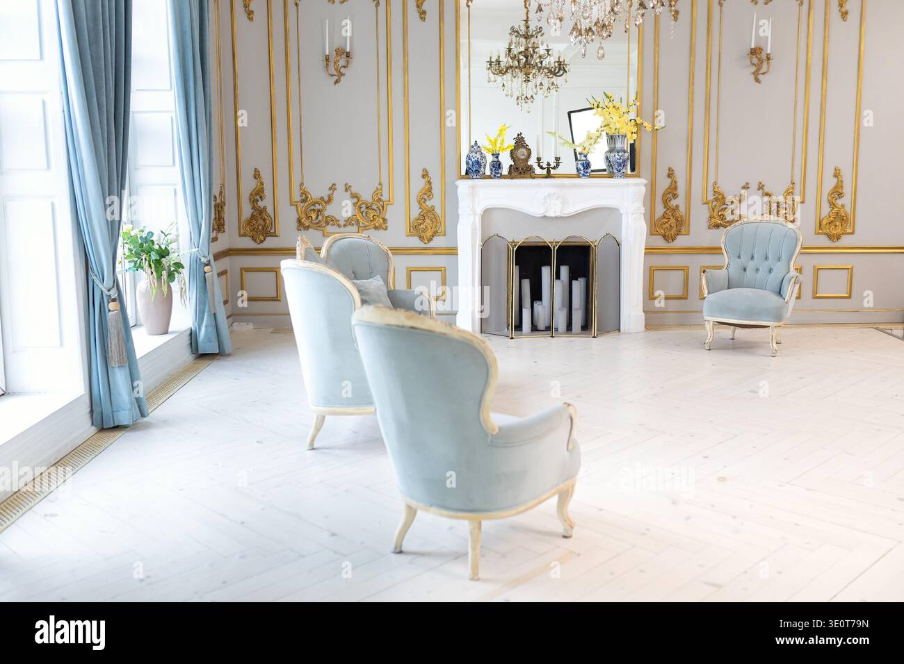 interni classici con eleganti poltrone, caminetto decorativo e lampadario di cristallo. Luminoso soggiorno in stile palazzo con mobili in velluto blu Foto Stock