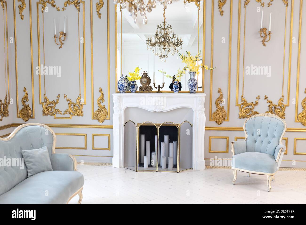 interni classici con eleganti poltrone, caminetto decorativo e lampadario di cristallo. Luminoso soggiorno in stile palazzo con mobili in velluto blu Foto Stock