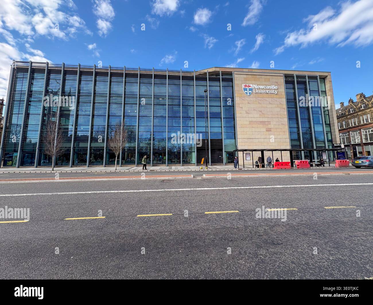 Newcastle, Regno Unito. 4 marzo 2026. Un edificio moderno con il logo della Newcastle University è visibile in una giornata di sole. La gente sta aspettando in una fermata dell'autobus Foto Stock