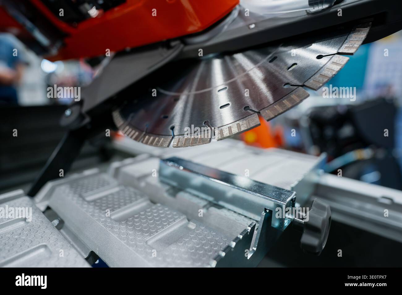 Primo piano di una lama per sega circolare segmentata su apparecchiature di taglio industriali, con piano di lavoro in metallo e guida visibile in una sala espositiva interna Foto Stock