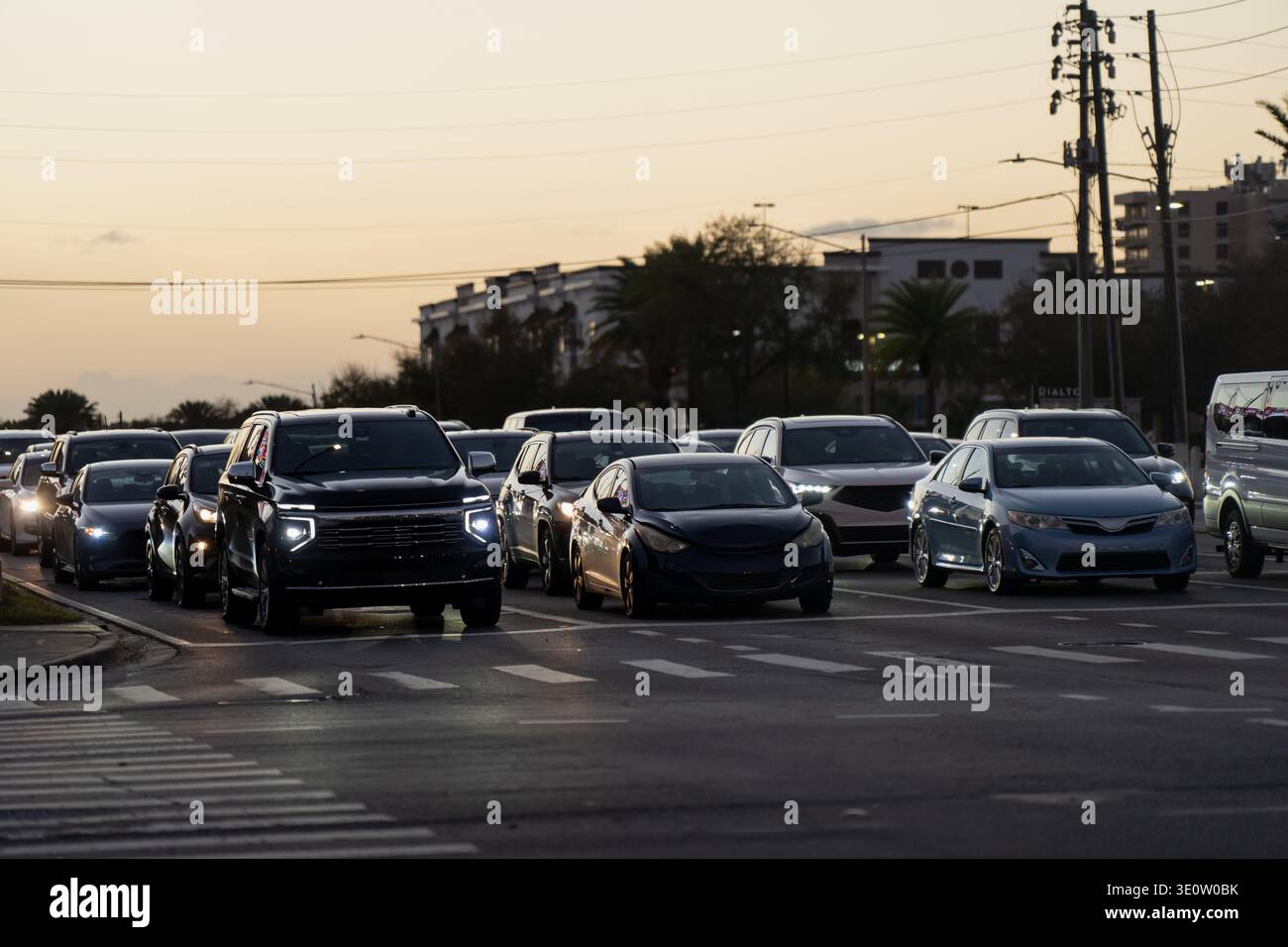 Il traffico serale della Florida si riempie di più corsie, con fari, berline e SUV che si avvicinano a un ampio incrocio urbano al crepuscolo di stasera Foto Stock