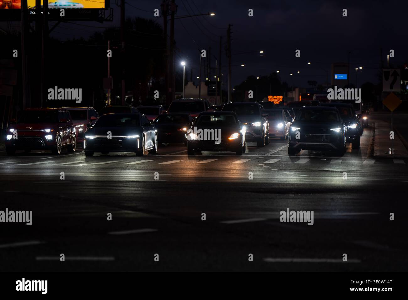Traffico notturno che si muove attraverso una strada urbana buia, con fari luminosi, auto multiple e asfalto riflettente bagnato sotto i semafori davanti alla strada Foto Stock