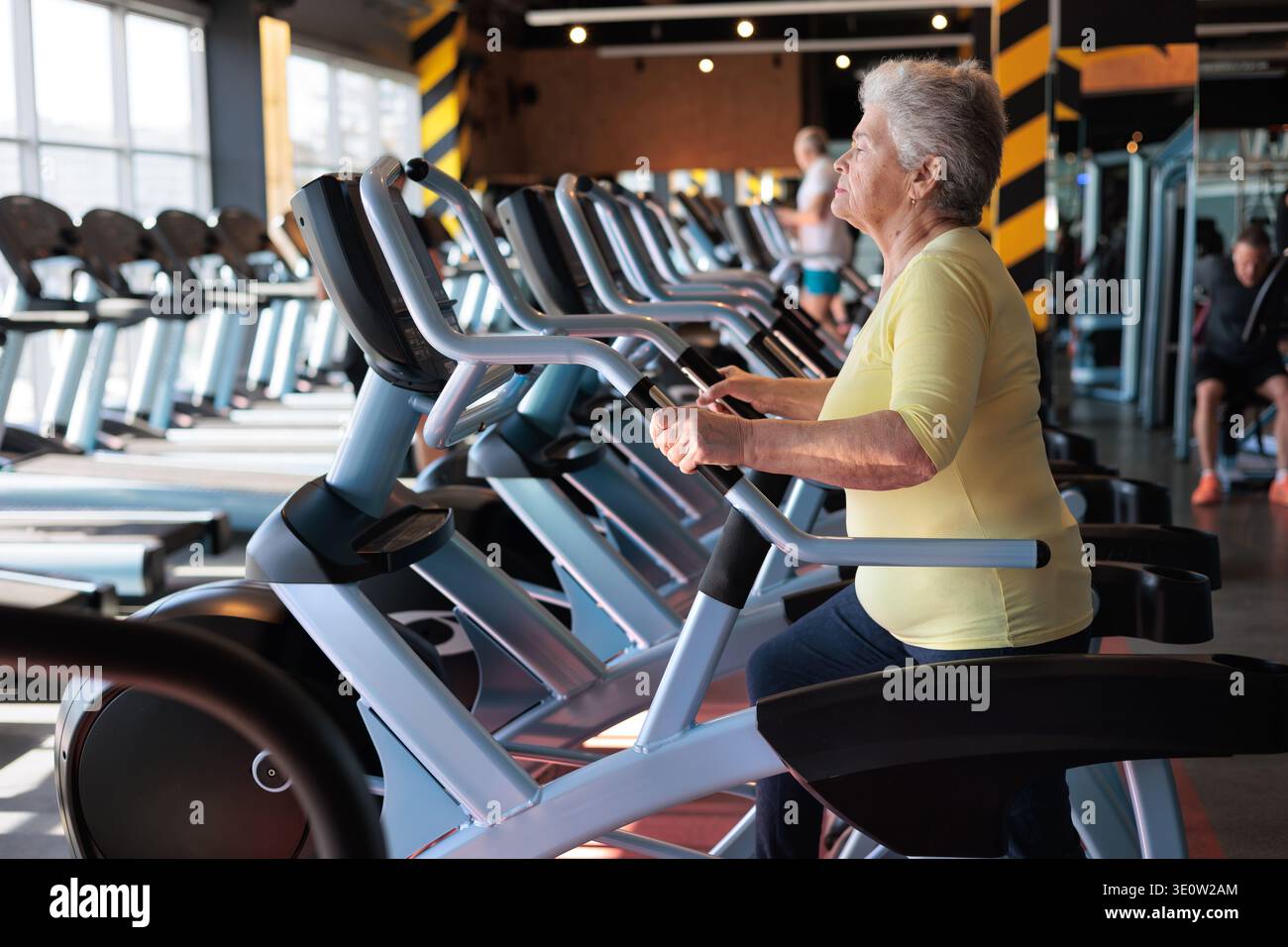 Fit donna anziana che utilizza l'ellittica Trainer in palestra, esercizio cardio a basso impatto per un invecchiamento sano Foto Stock
