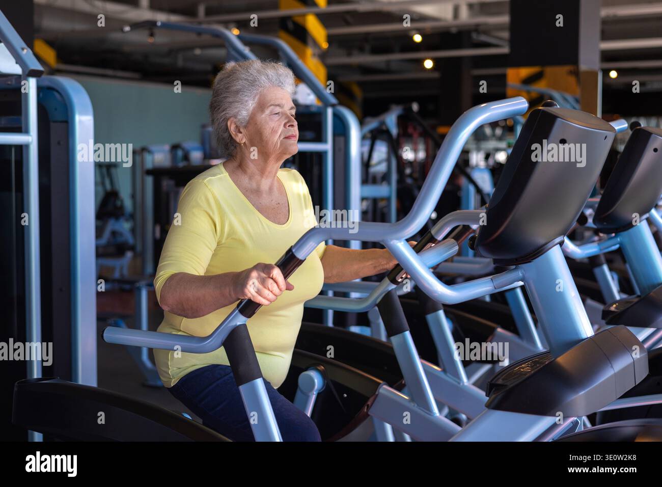 Fit donna anziana che utilizza l'ellittica Trainer in palestra, esercizio cardio a basso impatto per un invecchiamento sano Foto Stock
