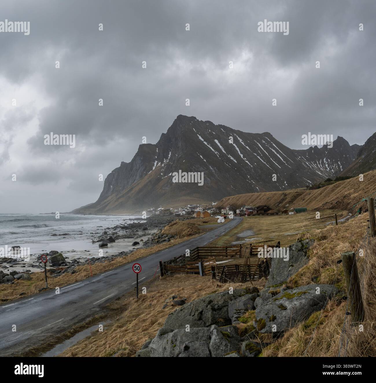 La strada che conduce al remoto villaggio costiero di Vikten sulle isole Flakstadøya Lofoten con le scogliere di Prekestolen sullo sfondo Foto Stock