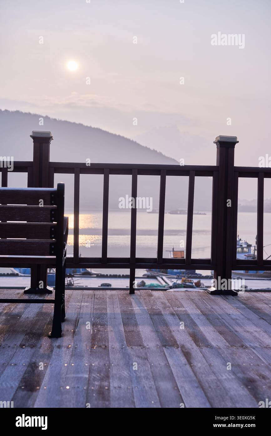 Tramonto malinconico al porto di Mangdeok, caratterizzato da un tranquillo ponte in legno, una panchina vuota e un caffe' vintage rosa sbiadito, che evoca nostalgia e solitudine. Foto Stock
