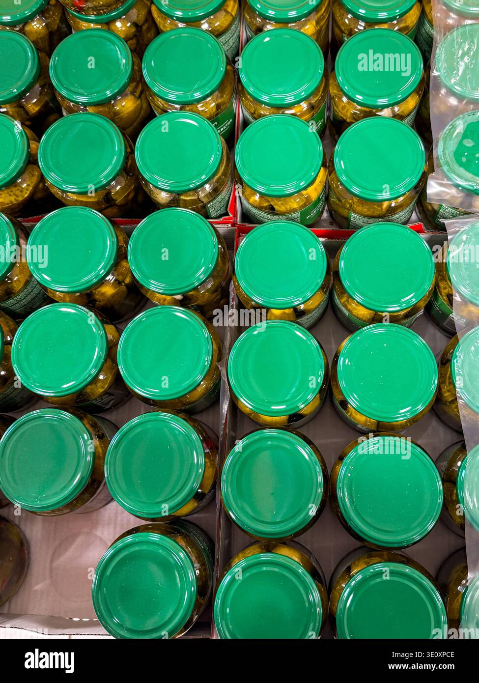 Valga, Estonia - 13 marzo 2026: Vista dall'alto di vari vasetti di cetrioli sottaceto disposti in scatole presso un supermercato. Ripetizione del verde Foto Stock