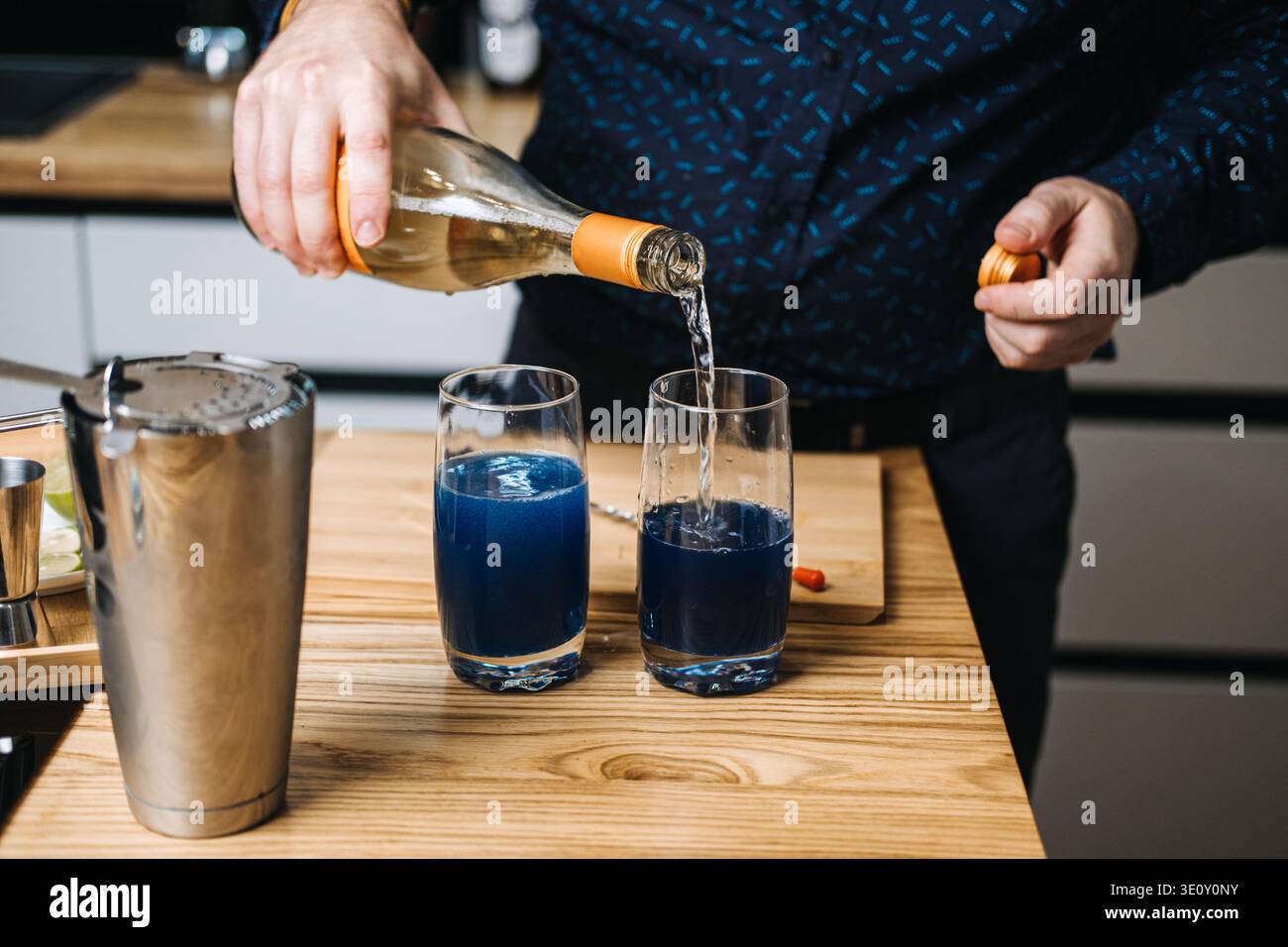 Versare il liquido dal flacone in bicchieri contenenti liquido blu sul bancone di legno. alcolici analcolici, cocktail a prova zero, alcolici Foto Stock
