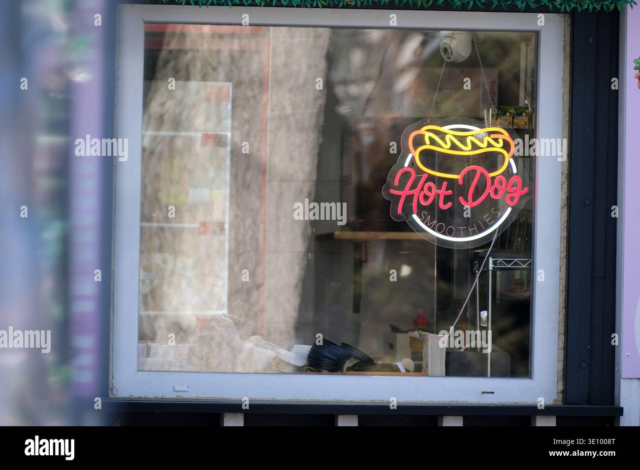 Un luminoso cartello al neon di hot dog splende alla finestra di un accogliente ristorante. Foto Stock