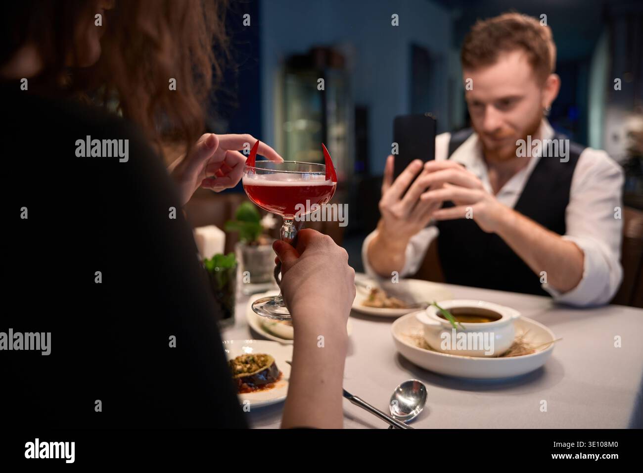 Coppia adulta che gusta un cocktail e fotografa il cibo al ristorante Foto Stock