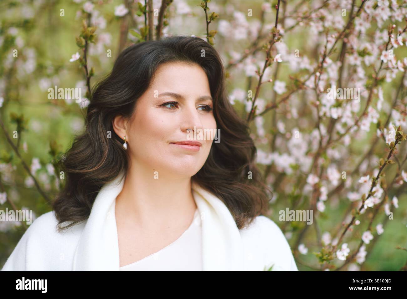 Elegante ritratto di donna tra rami primaverili in fiore, bellezza naturale con trucco morbido e capelli ondulati godendosi momenti tranquilli nel fresco giardino con del Foto Stock