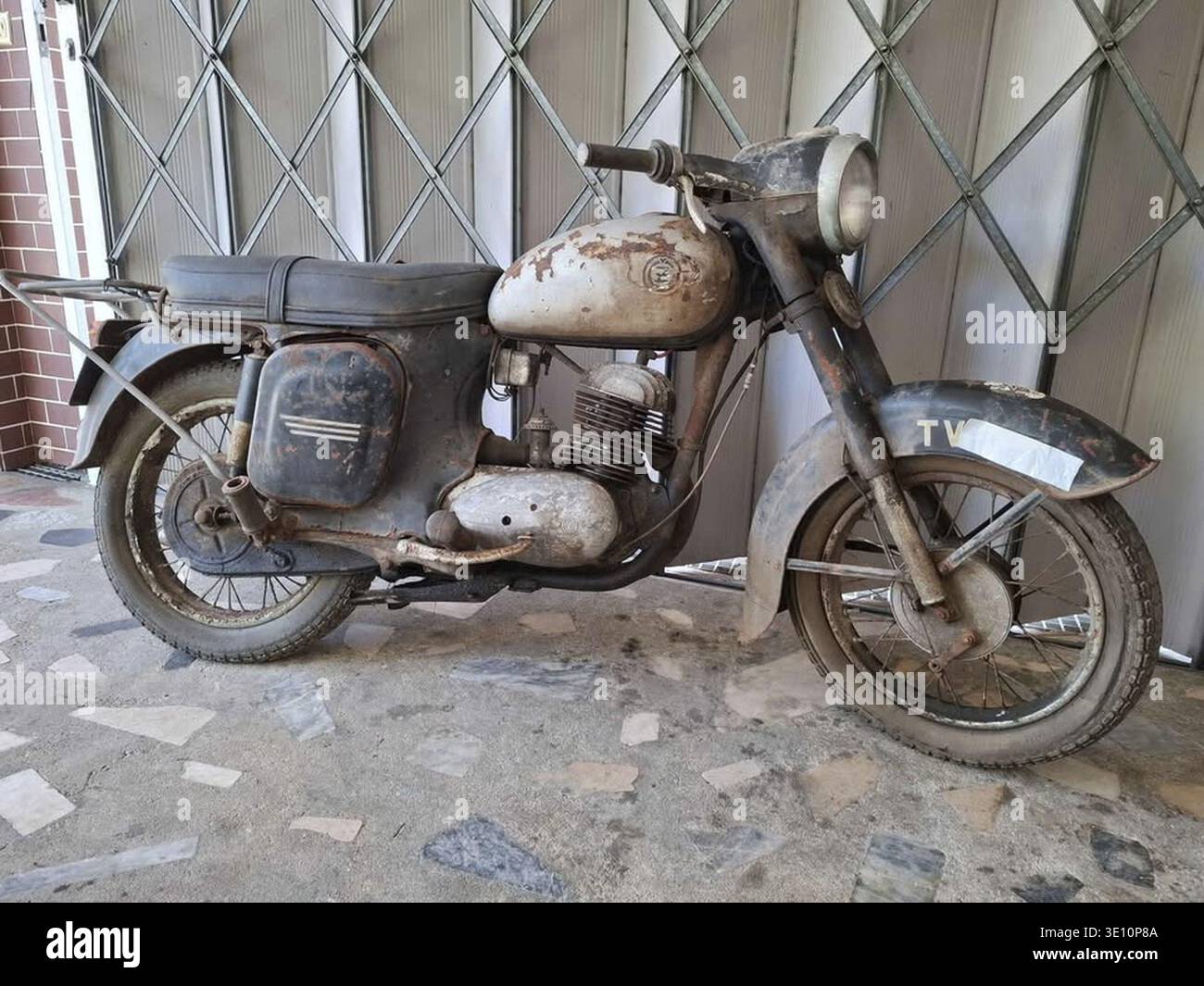 Vecchia e abbandonata moto Jawa seduta accanto ad un cancello metallico, mostrando segni di deterioramento avanzato Foto Stock