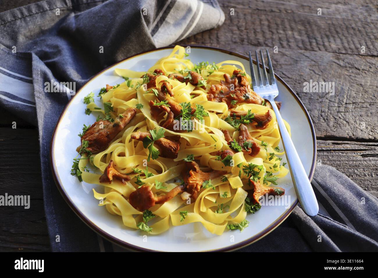 Tagliatelle fritte in funghi burro chanterelle con aglio e prezzemolo tritato finemente su tovagliolo a scacchi su sfondo rustico Foto Stock