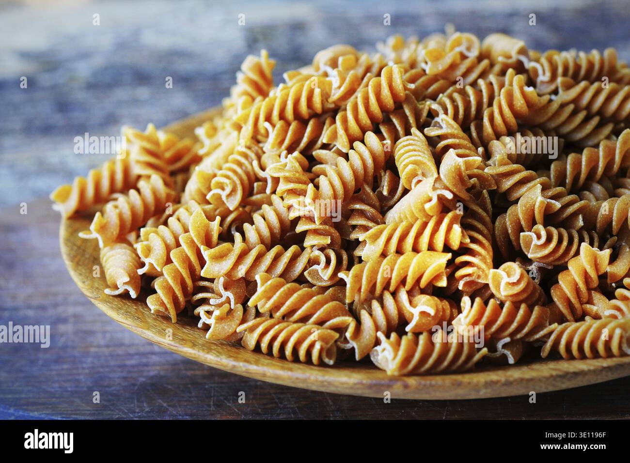 Fusilli integrali in un piatto. Pasta integrale su una tavola di legno Foto Stock