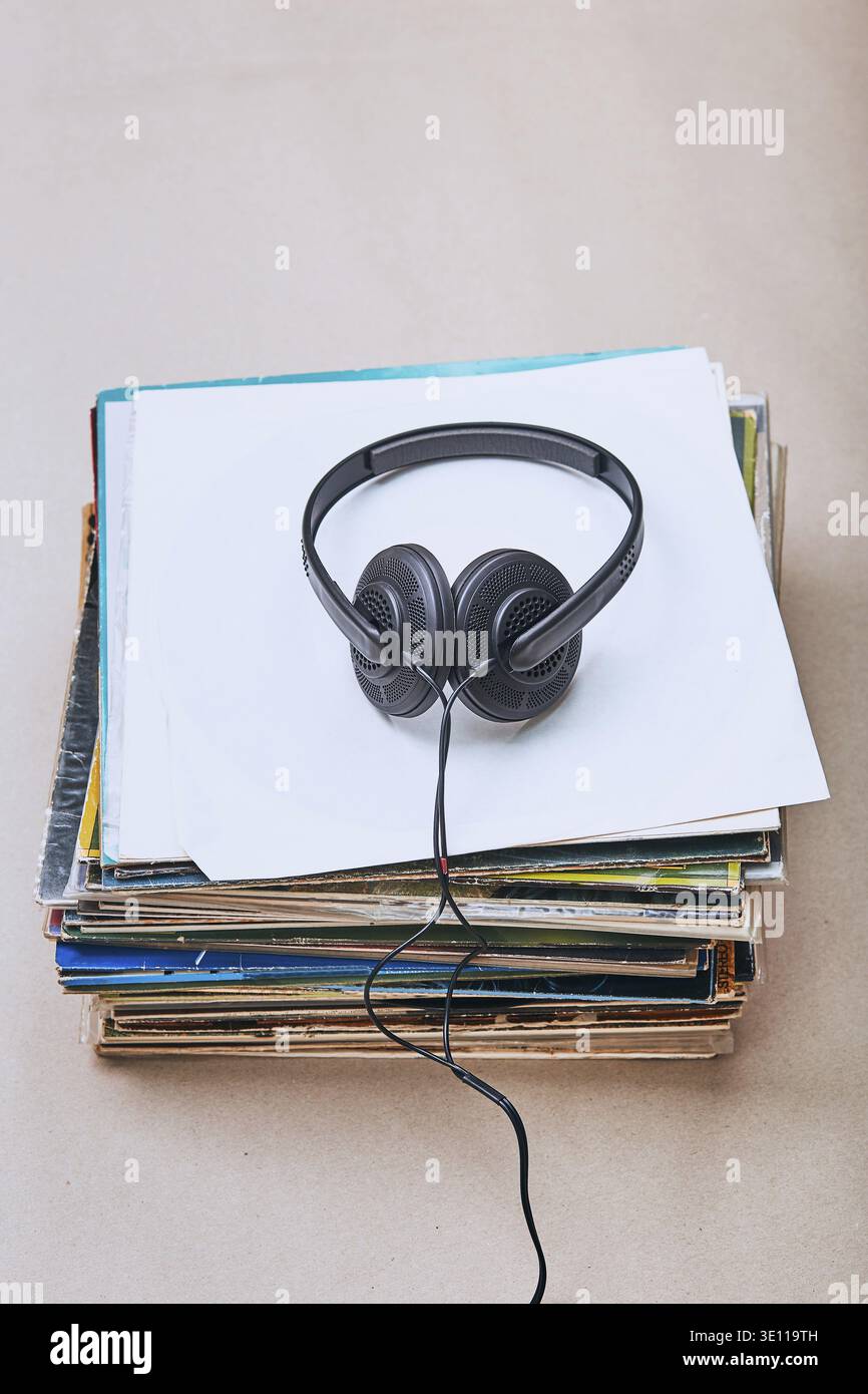 Stack di molti dischi e cuffie in vinile nero sulla parte superiore dello stack. Persone since, momenti reali, situazioni autentiche Foto Stock