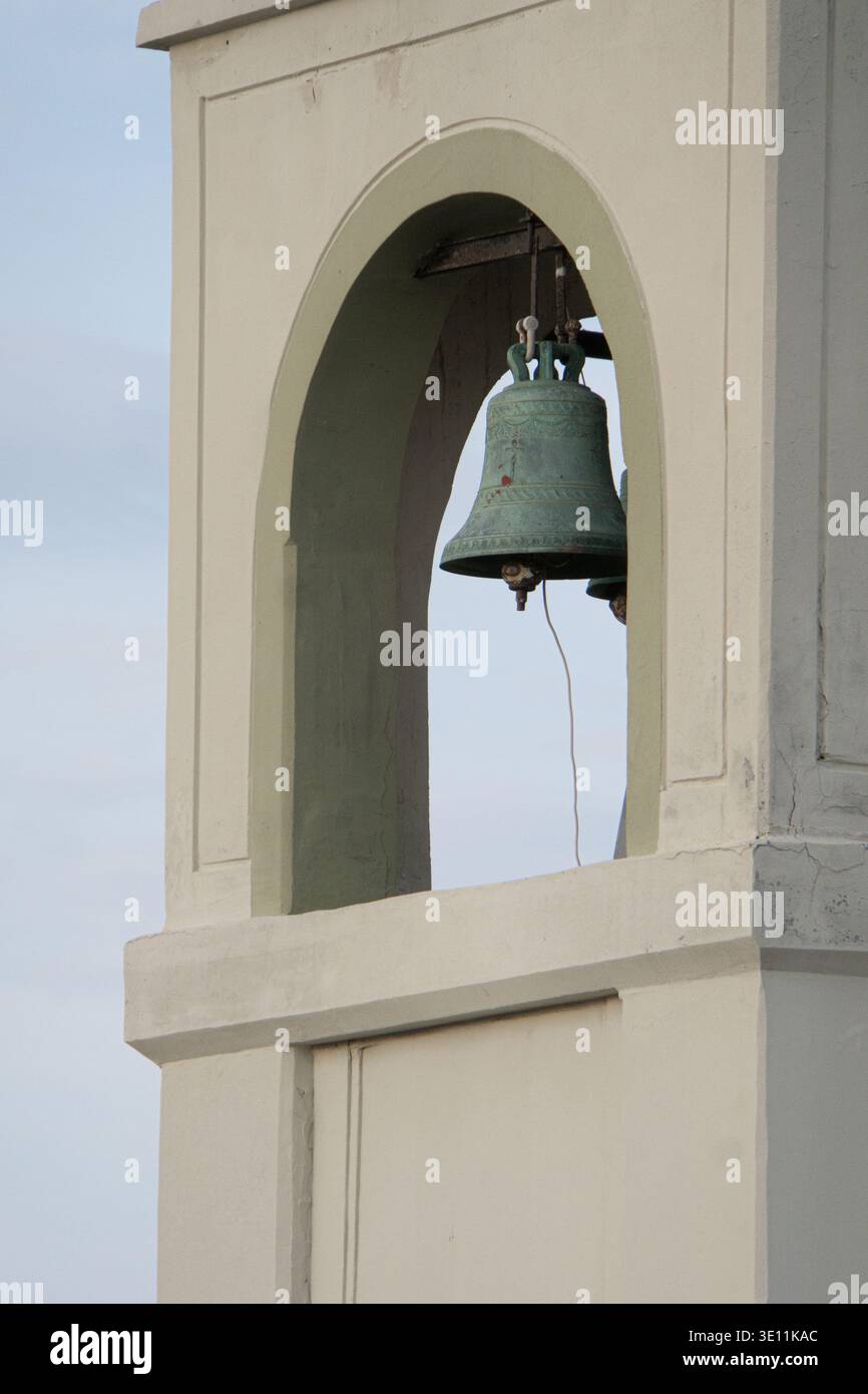 Campana della chiesa appesa all'interno di un arco a torre contro una nuvolosa sky.in Rodi, Grecia. Foto Stock