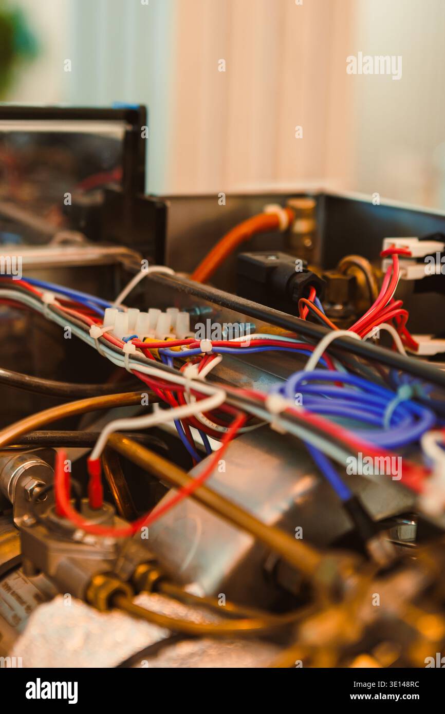 Un tecnico sta lavorando sulle parti interne di una macchina da caffè. Vari fili colorati sono collegati a diversi componenti. L'impostazione è occupata Foto Stock