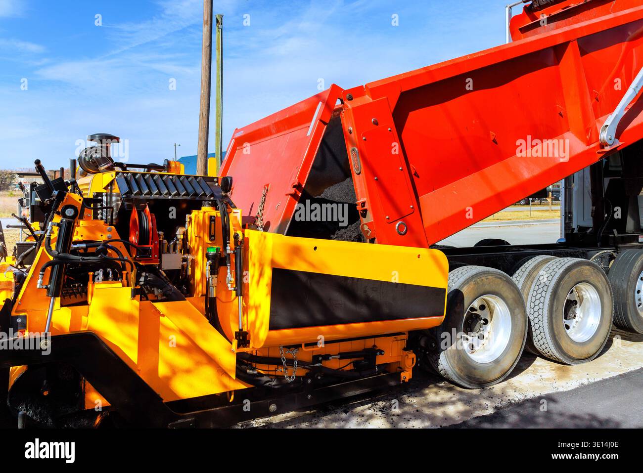 Il personale addetto alle costruzioni utilizza la macchina per pavimentazione mentre il dumper fornisce la miscela di asfalto per le riparazioni stradali Foto Stock
