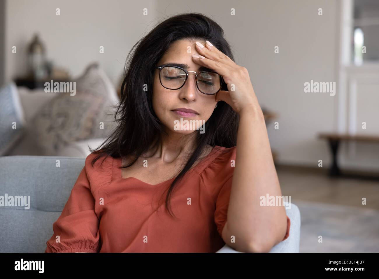 Donna stressata con gli occhi chiusi che toccano la fronte seduta all'interno Foto Stock