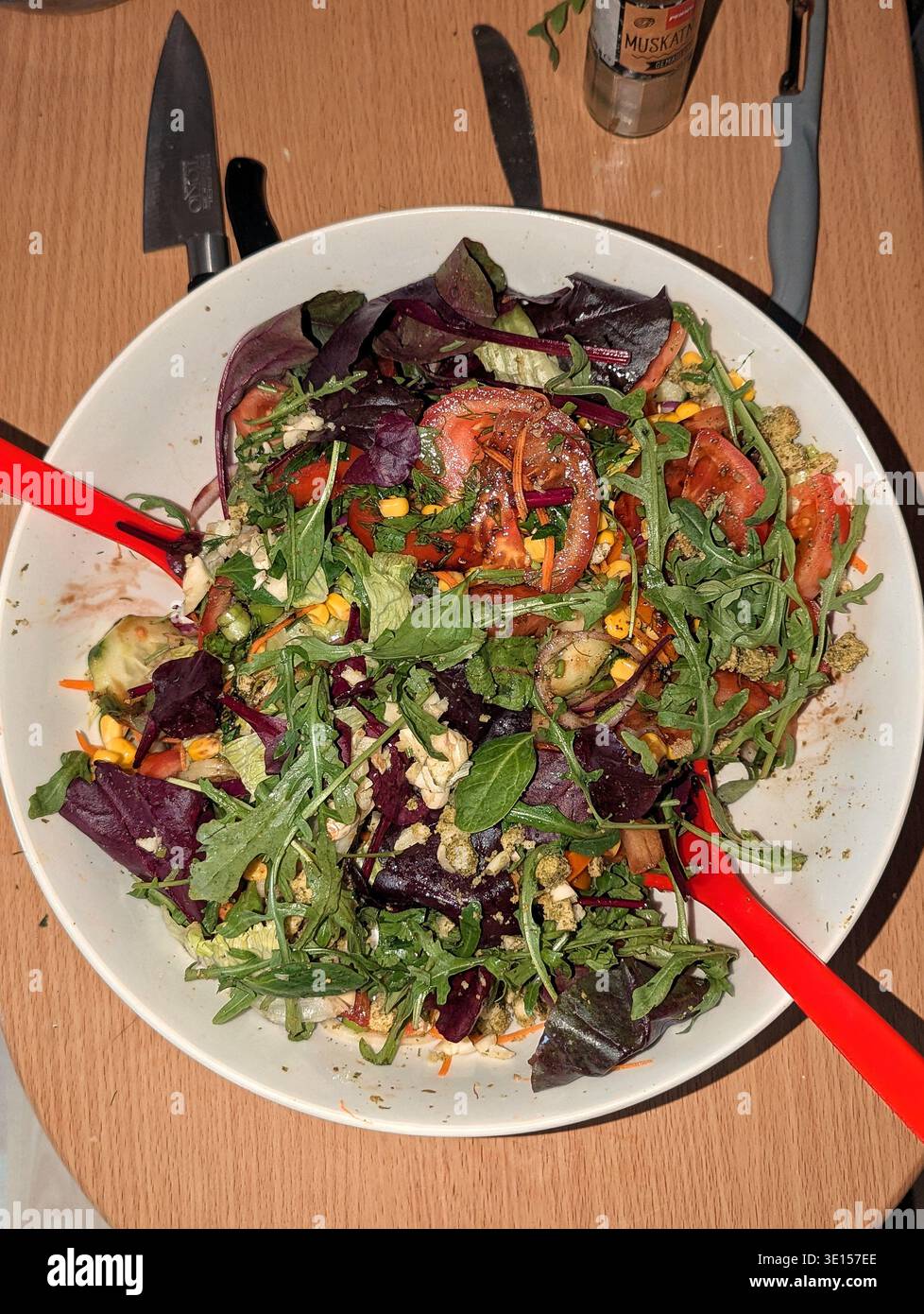 Ciotola per insalate di verdure miste vibranti con mais, pomodoro, cipolla rossa, rucola, radicchio, lanciato da Home Cook su un tavolo di legno per mangiare sano e preparare i pasti Foto Stock