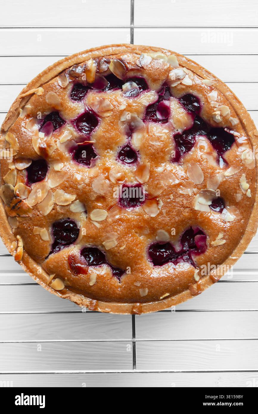 Torta bakewell alla ciliegia fatta in casa con mandorle, rinfrescata su uno sfondo di griglia di raffreddamento in metallo. Foto Stock