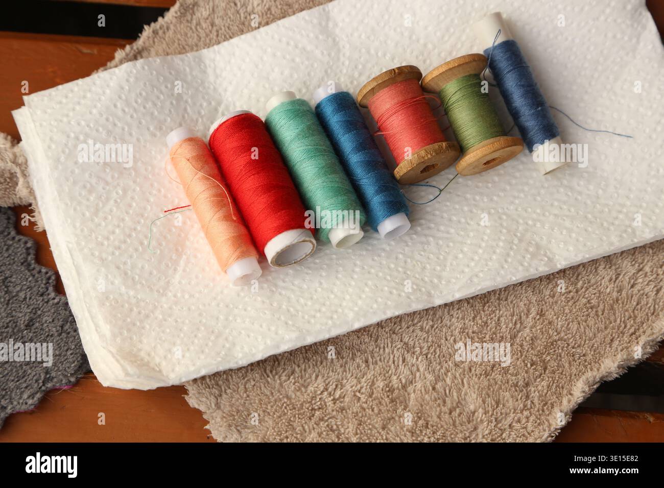 Le bobine di filettatura sono allineate su un tovagliolo di carta su un tavolo. Sono visibili colori e stili diversi. L'ambientazione sembra un'area di lavorazione in una casa, Foto Stock