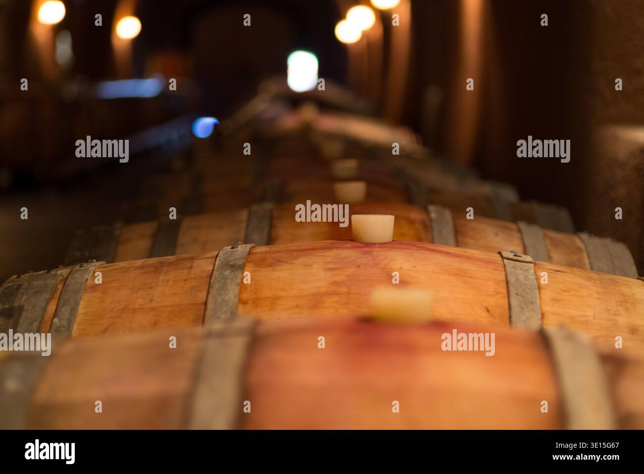 Una splendida foto ravvicinata che cattura una fila di botti di vino di quercia che invecchiano all'interno di una cantina poco illuminata nella Napa Valley, California. Foto Stock