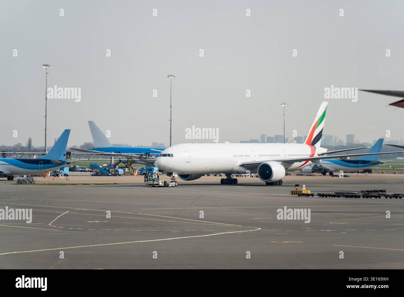 Grande aereo commerciale su un asfalto aeroportuale attivo circondato da attrezzature di assistenza a terra e altri jet, evidenziando la logistica delle compagnie aeree e inter Foto Stock