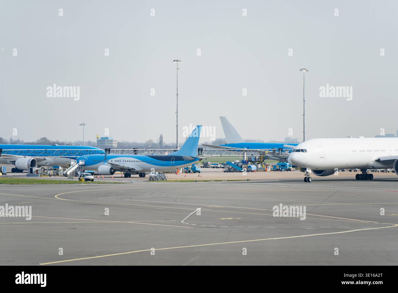 L'asfalto dell'aeroporto è affollato, con getti passeggeri parcheggiati e attività di servizio in background, evidenziando la capacità delle compagnie aeree, le reti di trasporto e la logistica Foto Stock
