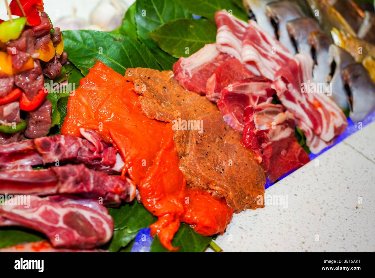 I piatti a base di carne cruda includono pollo marinato, pancetta di maiale, costolette di agnello, spiedini di manzo e filetti di pesce interi sono disposti su foglie verdi, pronte per l'uso Foto Stock